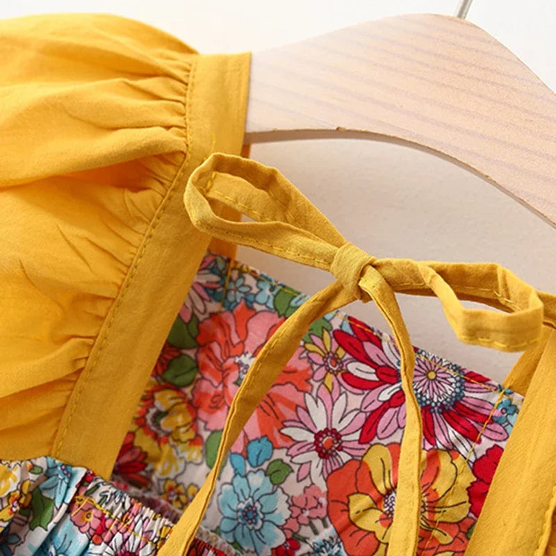 A yellow baby girl's dress with a floral print and matching yellow fabric tie-back details, displayed on a wooden hanger.
