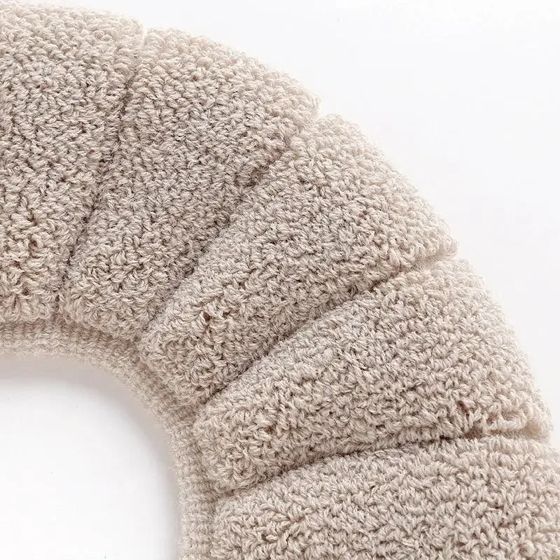 Close-up of a beige knitted soft acrylic toilet seat cover with ribbed texture.