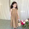 A young girl wearing a loose, sleeveless, beige cotton sundress with a gathered skirt and holding a woven basket of flowers.