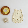 A cream-colored baby cotton sleeveless jumpsuit bodysuit set with small green leaves scattered across the fabric, next to a w