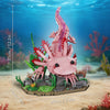 A pink sculpture of a dragon or sea creature is built on a base with green plants and coral in an underwater scene.