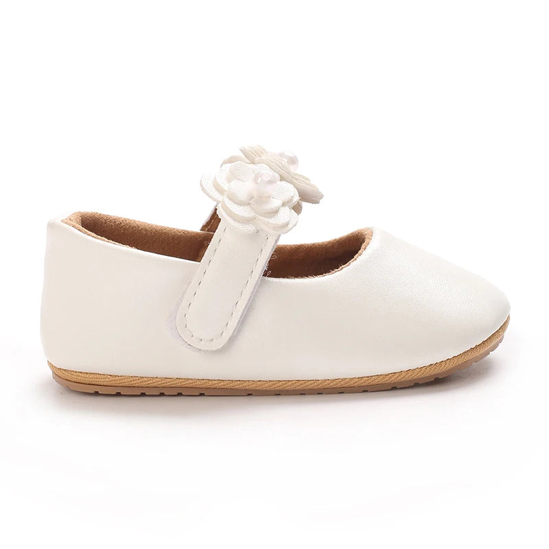 A pair of soft white baby first walker shoes with a decorative flower detail.