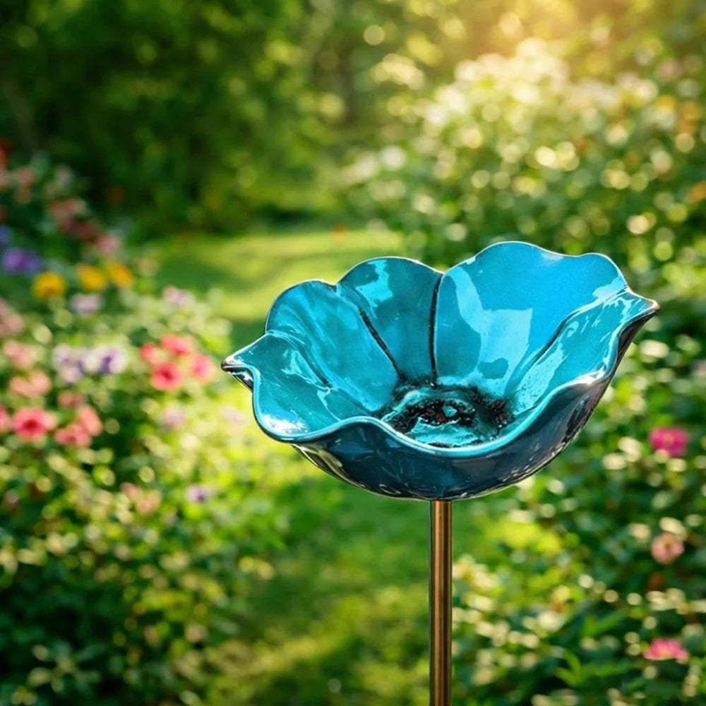 A handcrafted metal blue flower bowl or bird bath mounted on a stake in a lush garden setting.