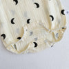 A close-up of a cream-colored baby cotton sleeveless jumpsuit bodysuit set with black crescent moon patterns.