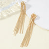 A pair of long, gold geometric tassel drop earrings displayed on a light background.