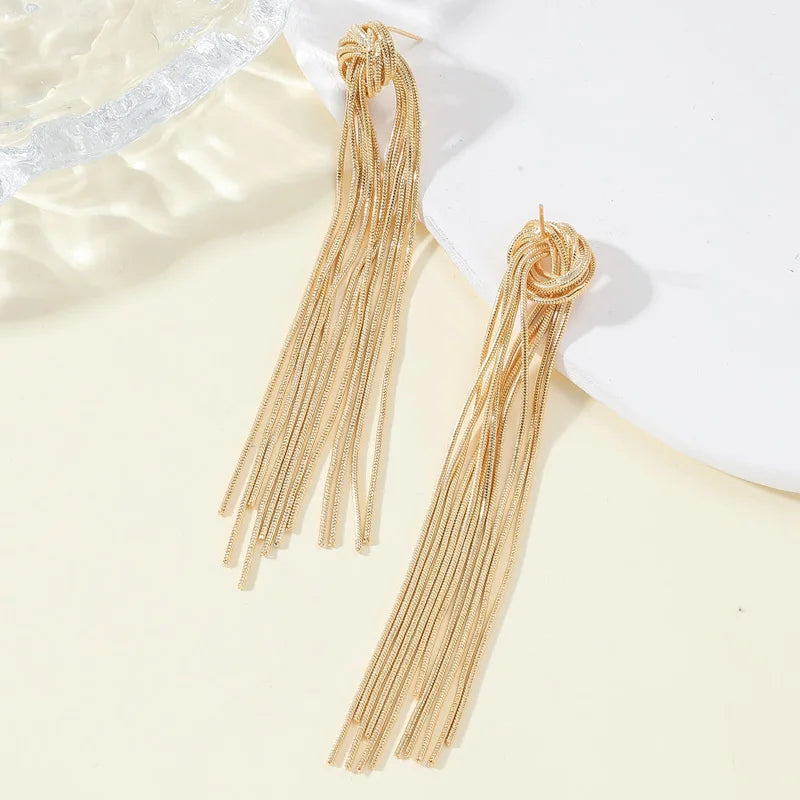 A pair of long, gold geometric tassel drop earrings displayed on a light background.