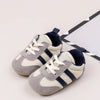 A pair of light gray and navy striped baby first walker shoes with white laces resting on a white background.