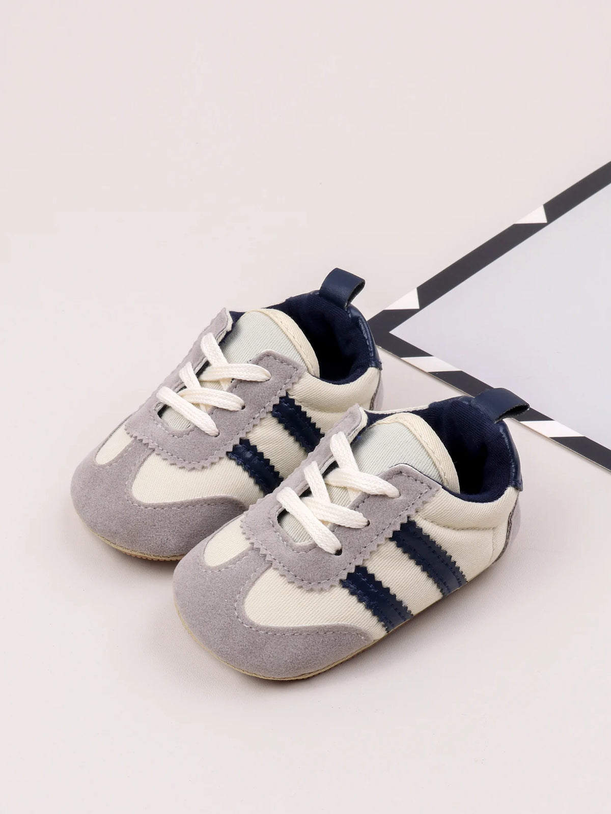 A pair of light gray and navy striped baby first walker shoes with white laces resting on a white background.
