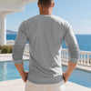 A man wearing a gray long-sleeve shirt standing outdoors by a pool and ocean view.