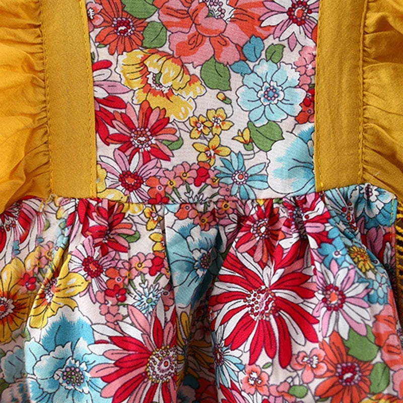 A close-up of a baby girl's floral print dress featuring pink, red, and yellow flowers with gold trim.