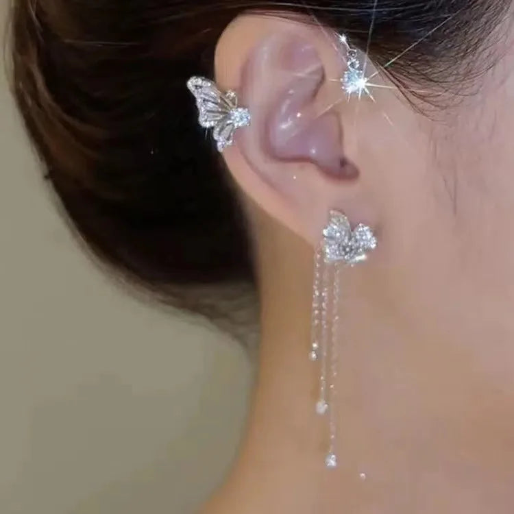 A close-up of a woman's ear showcasing a sparkling butterfly zircon ear cuff with a gold tassel earring.