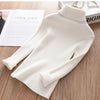 A white ribbed knit turtleneck sweater for kids displayed on a wooden surface.