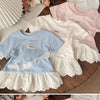 A light blue short sleeve cotton tee with white lace trim and a ruffled hem, displayed on a wooden surface.