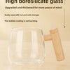 A clear borosilicate glass mug with a wooden handle is shown on a light wooden surface.