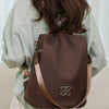 A brown nylon backpack with a silver logo is worn by a person in a light green shirt.