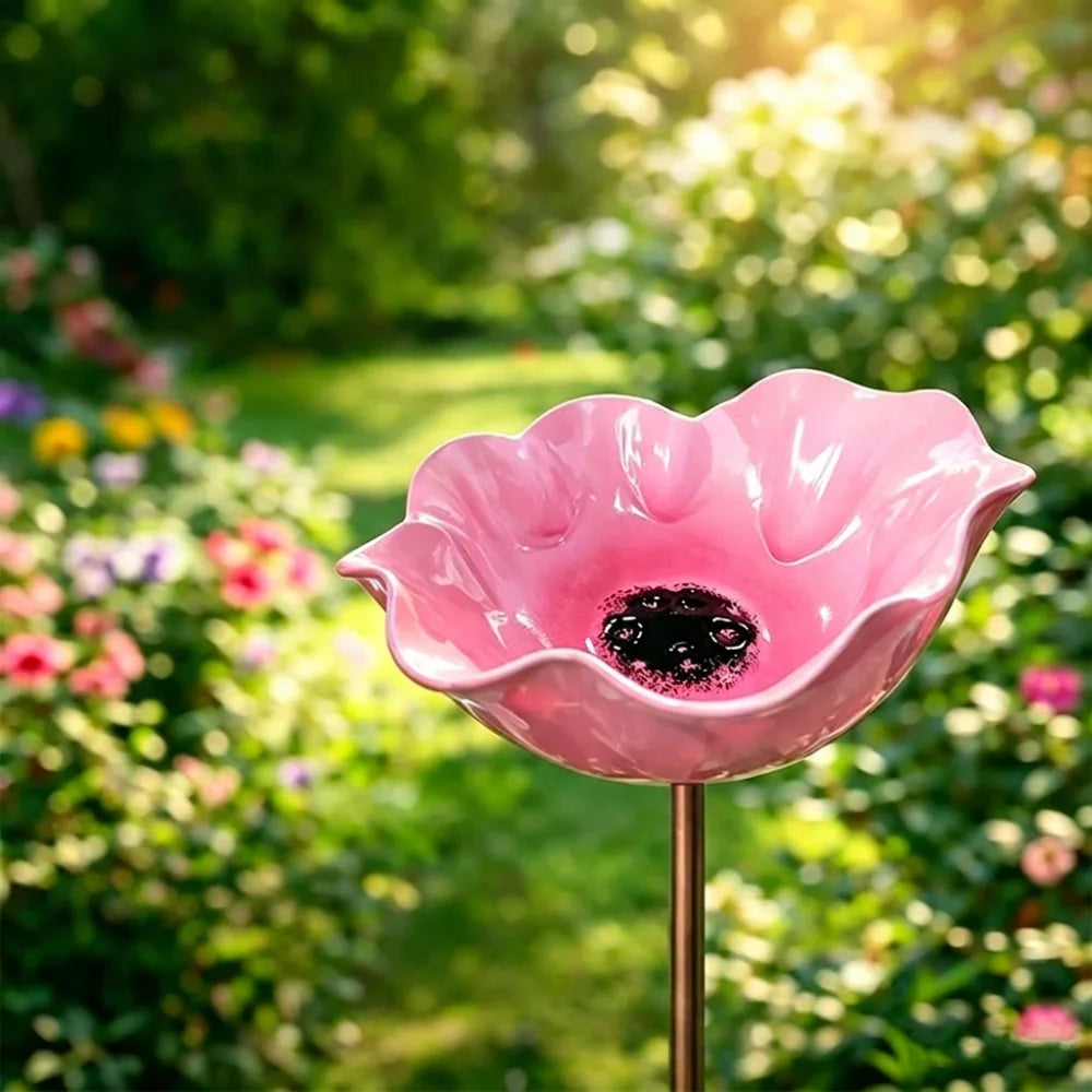A pink handcrafted metal flower garden stake with a bird bath sits in a lush green garden setting.