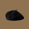 A black wool beret hat is shown against a solid brown background.