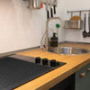A silicone stove protector mat is placed on a wooden countertop in a kitchen setting.