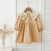 A beige kids princess dress with floral embroidery and lace trim hanging on a white wooden hanger.