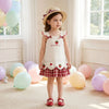 A young girl wearing a white pinafore dress with strawberry and bunny print, standing in a bright room surrounded by balloons
