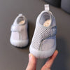 A hand holds a pair of white breathable baby first walker shoes for toddlers.