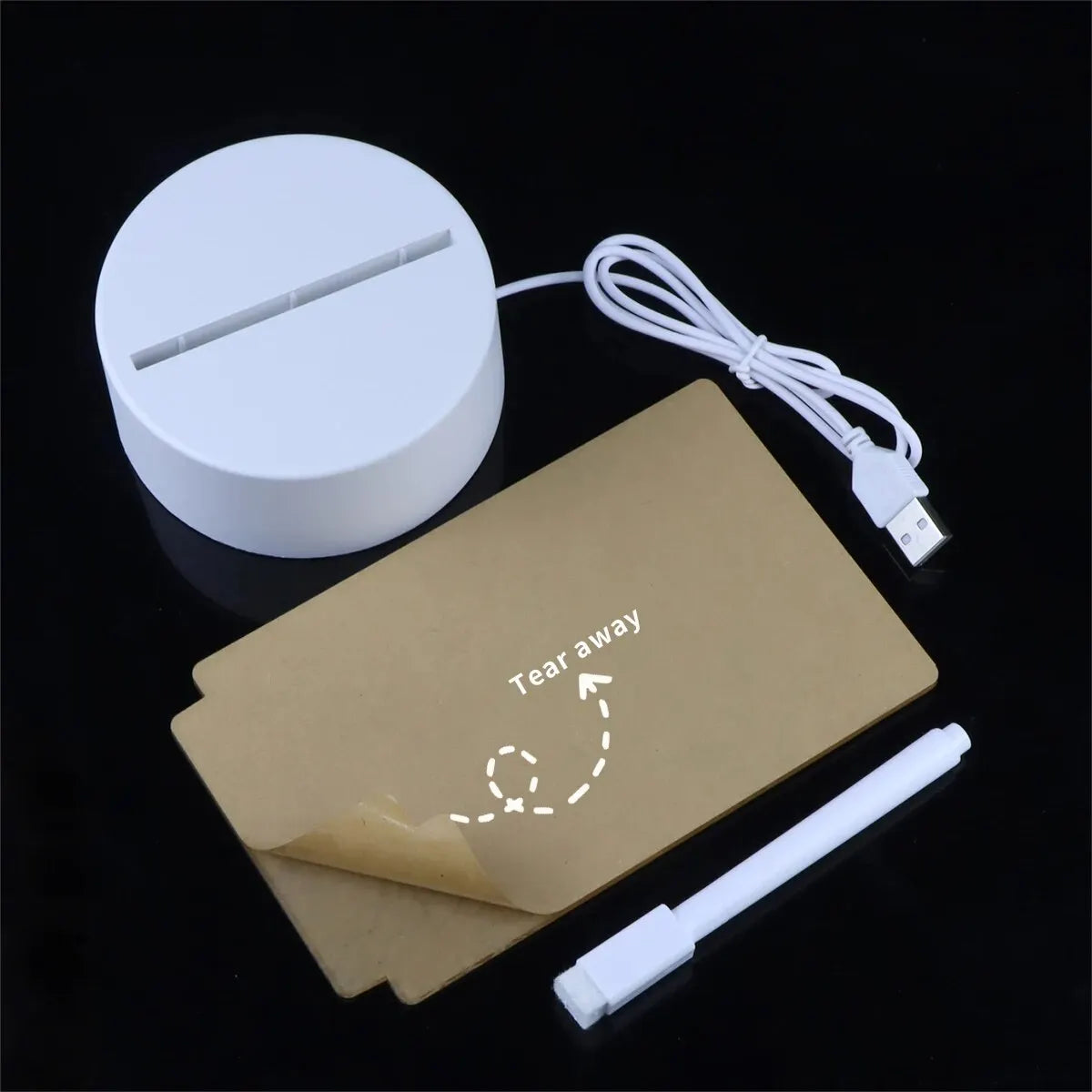 A white acrylic message board desk lamp with a pen and power cord on a black surface.