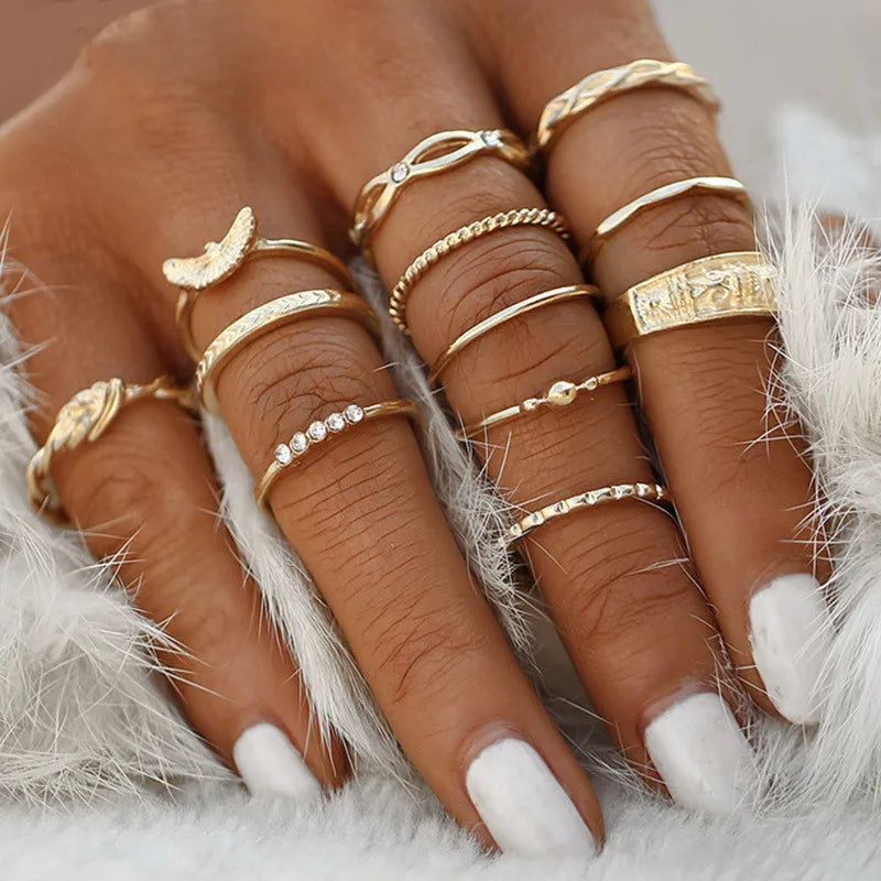 A hand wearing a set of boho gold rings featuring vintage geometric, cross, pearl, and butterfly designs.