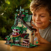 A young boy is looking at a detailed building block set depicting a farm scene with green monster figures.