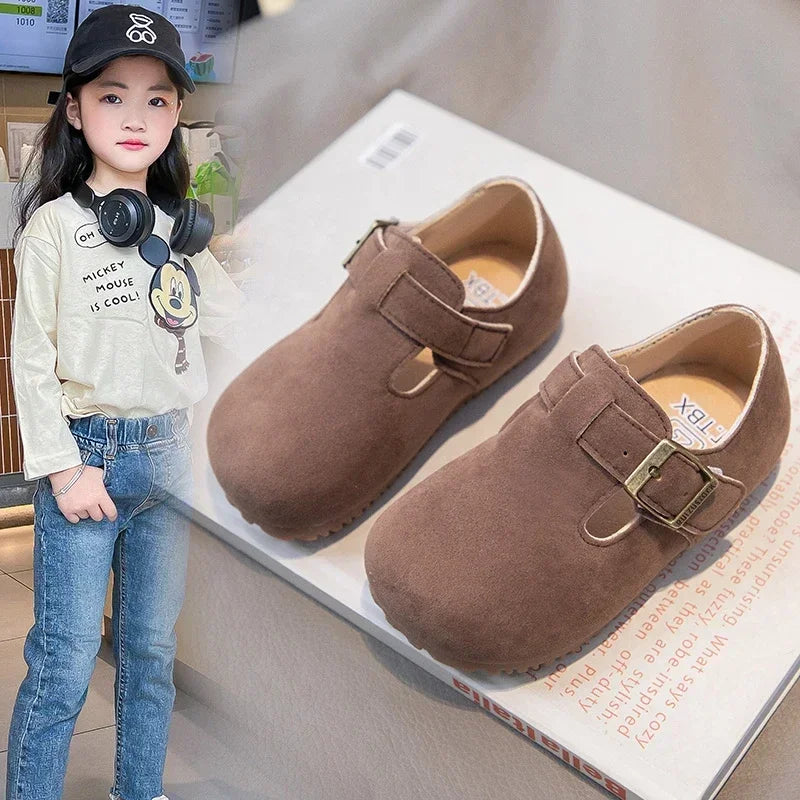 A young girl models brown retro non-slip kids' moccasin shoes with hook-and-loop closure.