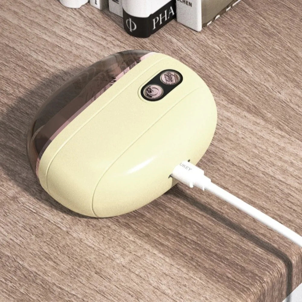 A beige electric nail clipper and grinder with a clear top is resting on a wooden surface.
