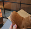 A hand holds a brown suede kids winter ankle boot with a plush lining.