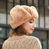 A woman wearing a beige fur-lined Russian ushanka trapper hat and a cream knit sweater.