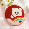 Cara de oso tejida a mano o crochet con cuerpo naranja y diseño arcoíris en un aro de bordado redondo.