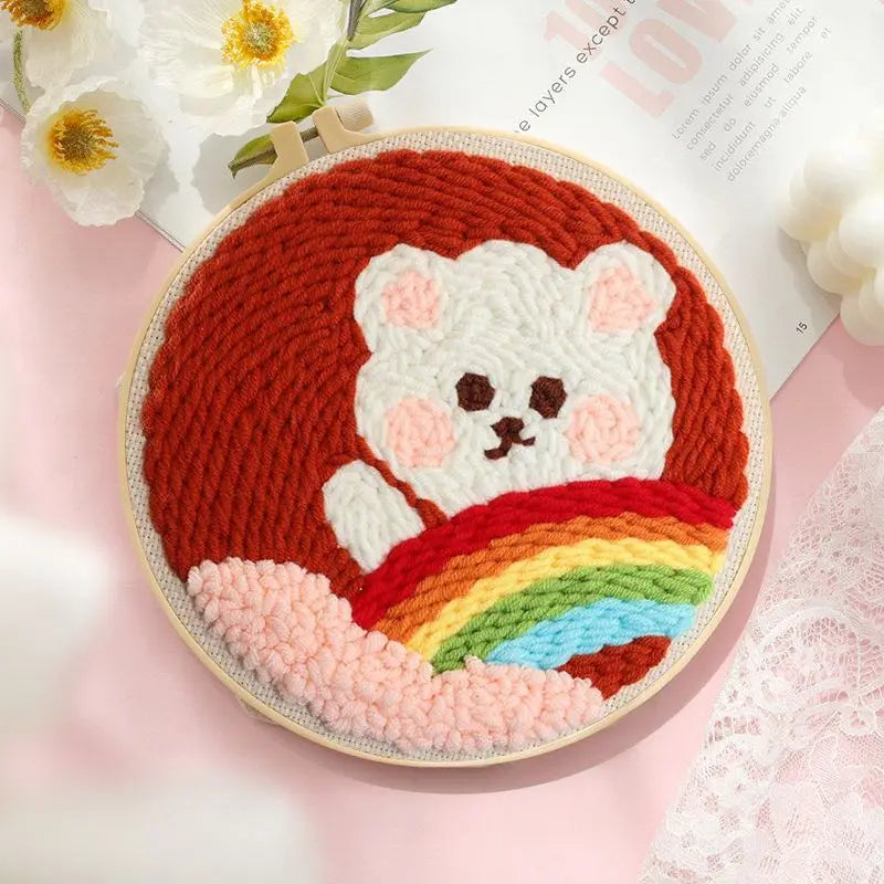 Cara de oso tejida a mano o crochet con cuerpo naranja y diseño arcoíris en un aro de bordado redondo.