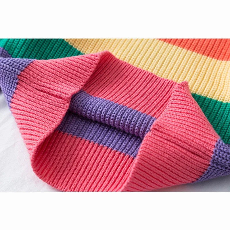 A close-up of a girls' rainbow striped knit sweater showing pink, purple, and yellow stripes.