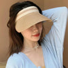 A woman wearing a beige woven straw sun hat with a wide brim and a delicate gold chain necklace.