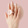 A hand holds a pink bath sponge with a white suction cup on a light pink textured surface.