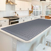 A gray silicone stove protector mat is placed on a kitchen countertop, ready for use on cooktops.