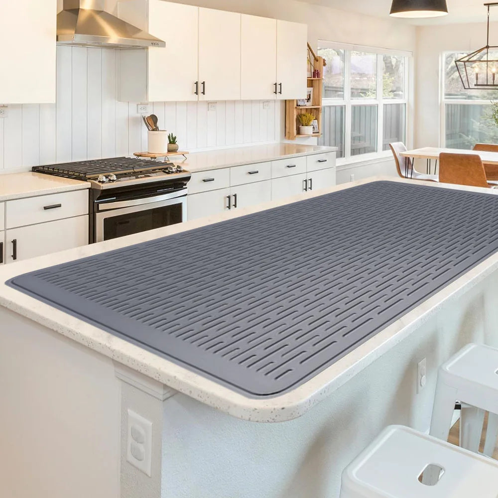 A gray silicone stove protector mat is placed on a kitchen countertop, ready for use on cooktops.