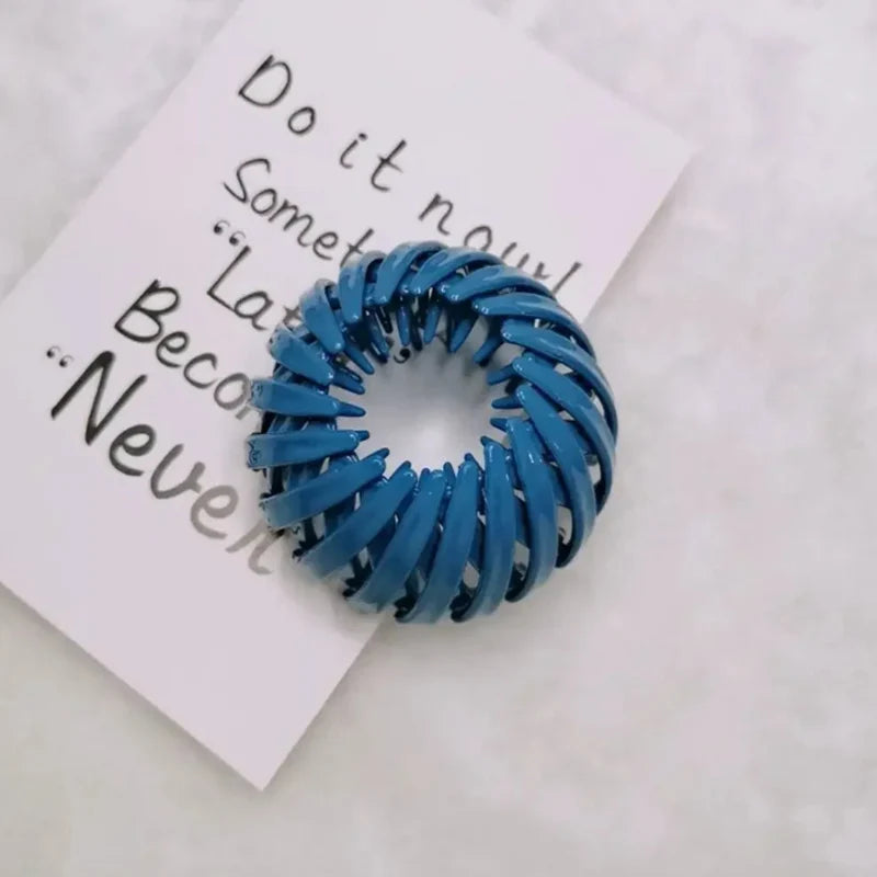 Nærbilde av en blå hårklips i spiral til hestehaler på et hvitt kort med tekst.
