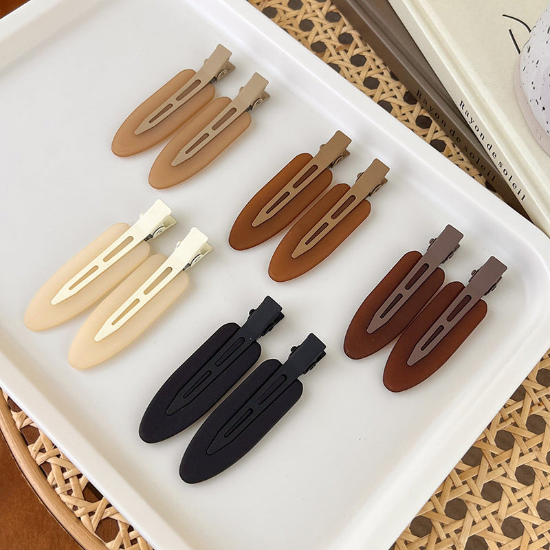 A set of six matte resin side hair clips in various shades of brown and beige displayed on a white tray.