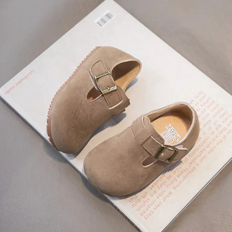 A pair of tan retro non-slip kids' moccasin shoes with an easy hook-and-loop closure resting on a white card.