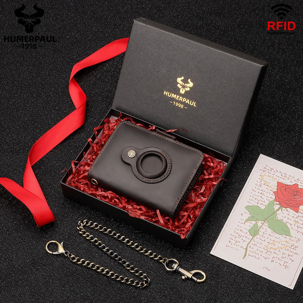 A black leather smart wallet with a ring holder and a chain is displayed inside a wooden box with red shredded paper.