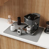 A silicone stove protector mat is placed on a countertop next to an electric kettle and a small dark jar.