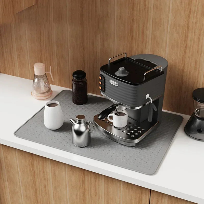 A silicone stove protector mat is placed on a countertop next to an electric kettle and a small dark jar.