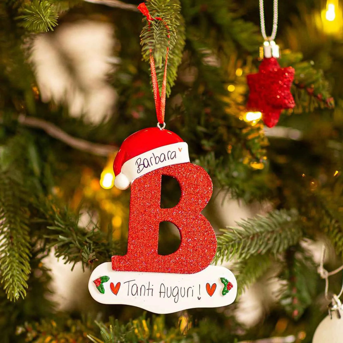 Rød glitrende akrylbokstav B med personlig melding hengende på juletre.