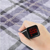 A hand holds a black digital blood pressure monitor displaying 0.00, resting on a plaid fabric background.