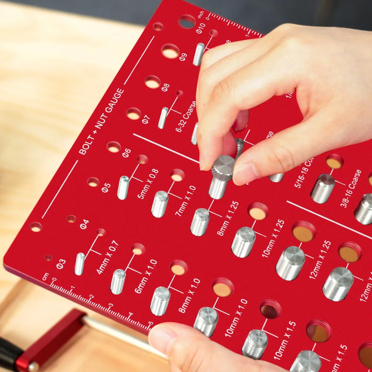 A hand is using a red bolt and nut thread identifier gauge to measure various standard sizes of bolts and nuts.