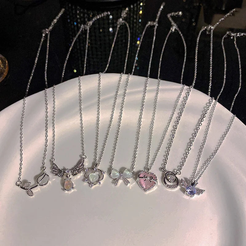 A display of silver crystal bow angel wings heart pendant necklaces arranged on a white plate.