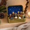 A gold-colored metal tin box containing a classic nativity scene with figures and a blue starry background.